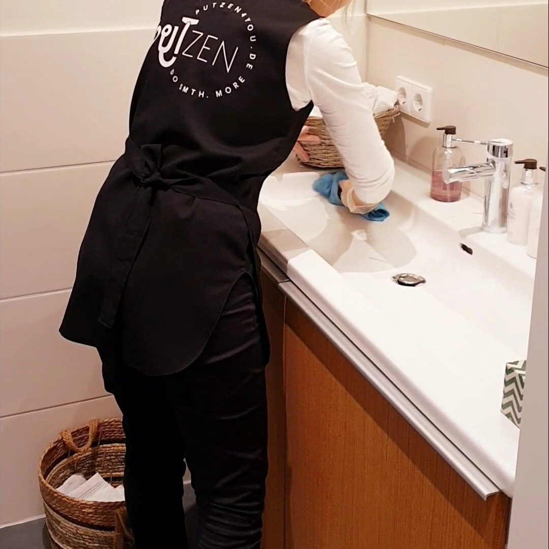 Person in Putzen4YOU uniform cleaning a sink with dry cloth